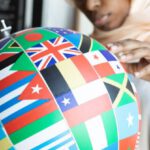 International Study - Concentrated African American female in traditional Muslim clothes and eyeglasses finding flag of country on globe